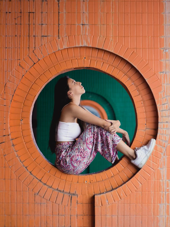 Young woman sitting in round brick opening, embracing a moment of reflection in George Town.